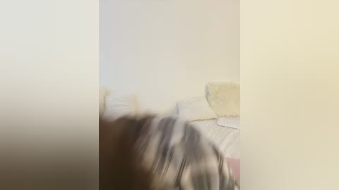 A blurred video of a person, possibly a child, lying on a bed with white bedding and a pillow. The background is softly lit, creating a hazy, out-of-focus effect.