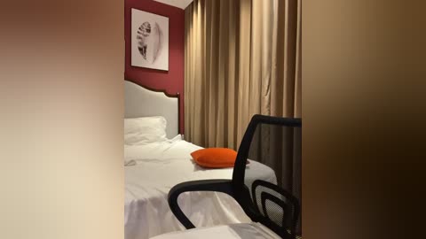 Video of a modern hotel room with a white bed, beige curtains, red wall, black office chair, and orange pillow.