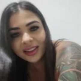A blurred video of a young woman with long, dark hair, light skin, and a tattoo sleeve on her left arm, smiling slightly.