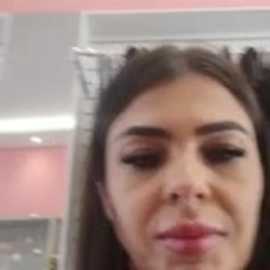 Video of a close-up of a woman with long, dark hair, wearing heavy makeup, including dramatic eyeliner and mascara, and a light pink lip color, against a pink and white background.