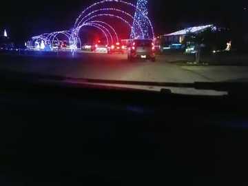 Media: Video of a nighttime amusement park with glowing, multi-colored arches and rides, illuminated by festive lights. The scene is dark, with the lights creating a vivid contrast.