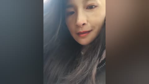 Video of a young Asian woman with long, straight black hair, fair skin, and a slight smile, partially visible in a dimly lit room.