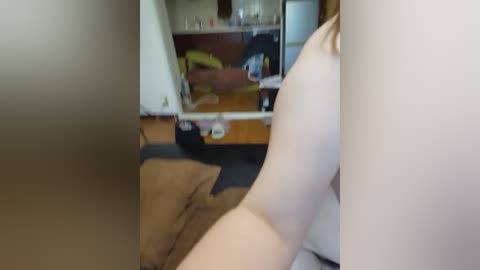 A video captures a woman's arm and hand with a light tan complexion, partially reflected in a mirror, amidst a cluttered bedroom with wooden furniture and a brown rug.