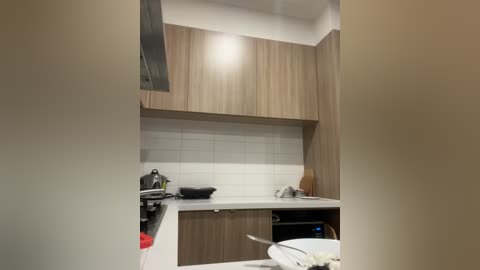 A video of a modern, minimalist kitchen with light wood cabinets, white subway tile backsplash, black stove, stainless steel appliances, and a white countertop.