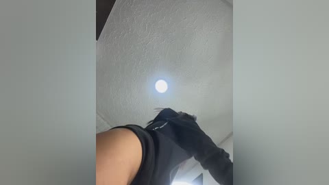 Video of a person wearing black gloves and a black shirt, standing on a white ceiling with a bright light source shining down, creating a halo effect.