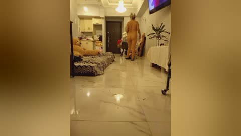 Video of a modern, dimly-lit living room with polished marble floors. A nude elderly woman walks toward a sofa where another nude elderly woman sits, both with gray hair.