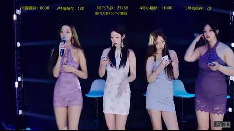 Video of four women in purple and white dresses, singing into microphones on a stage, with a dark background and LED screens displaying Japanese text.