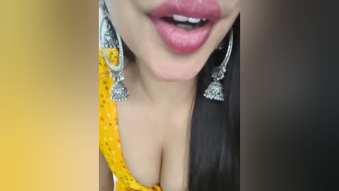 Video of a woman with full, pink lips, wearing a yellow blouse and large, silver earrings. Her skin is light brown, and she has long, straight black hair.