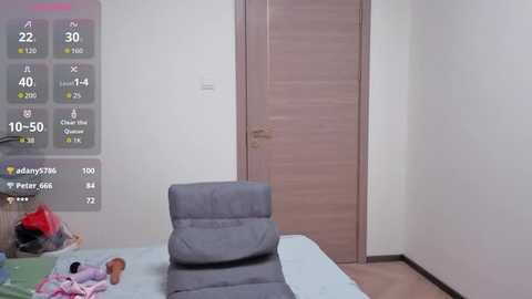 A video of a minimalist bedroom with a grey recliner, a closed wooden door, and a bed with colorful pillows. The image is overlaid with digital statistics and a user's name.