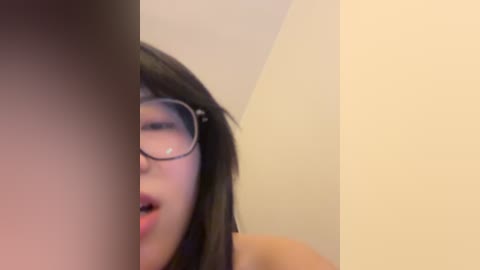A blurry video featuring a young Asian woman with long black hair, glasses, and a slightly open mouth, partially obscured by a vertical, dark object.