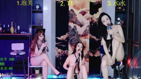 A video of three nude Asian women with long hair, singing into microphones in a dimly lit room with a large, abstract artwork in the background.