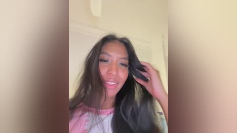 Video of a young Asian woman with long, straight black hair, light skin, and a slight smile. She's wearing a tie-dye shirt and is indoors, partially obscured by a blurred wall.