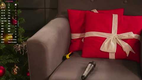 Video of a gray sofa with a red pillow adorned with a white ribbon, a screwdriver on the cushion, and a Christmas tree with ornaments in the background.