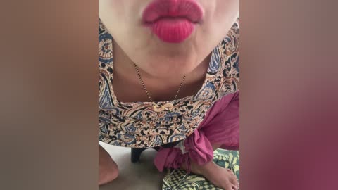 A video showing a close-up of a woman's face and neck, with full red lips, intricate patterned blouse, and a gold necklace.