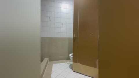 Video of a modern bathroom with beige walls and white-tiled floor. A wooden door and a white toilet are partially visible. The lighting is soft and ambient, creating a clean, minimalistic ambiance.