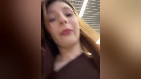 A video of a Caucasian woman with light skin and shoulder-length brown hair, wearing a maroon top, standing in an indoor setting with beige walls and a ceiling grid.