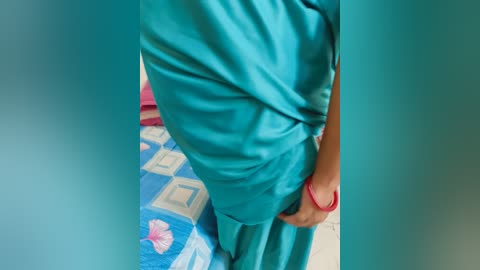 Video of a person wearing teal scrubs, standing in a room with a blue and pink patterned rug.