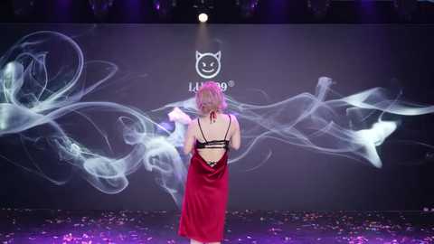 Video of a blonde woman in a red dress, back to the camera, on a dark stage with swirling white smoke and the \"ALIBABA\" logo.