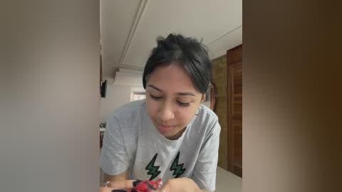 Video of a young South Asian woman with black hair, wearing a gray T-shirt with green lightning bolt design, holding a bowl of red grapes.