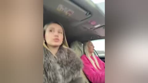 Video of two blonde women in a car, one in a fur coat, the other in a pink hoodie.