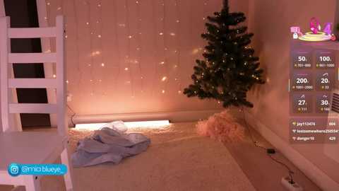 Media: A video of a cozy, dimly lit room with a white Christmas tree and a pile of clothes on the floor. The background features a large window with soft, warm lighting.
