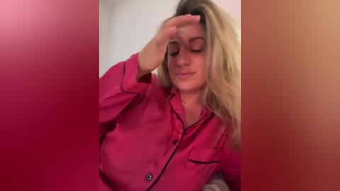 A video of a blonde woman in a pink button-up shirt, shielding her eyes with one hand, standing against a gradient background of red, orange, and white.