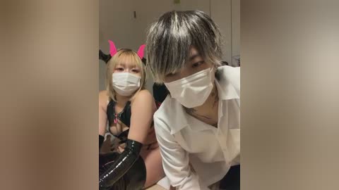 Video of two women in a dimly lit room; one in a pink bunny costume, the other in a white mask and lab coat, both wearing face masks.