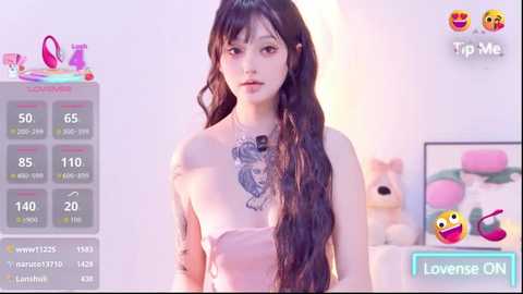Video of a slender, light-skinned woman with long, wavy black hair and a large, detailed tattoo on her chest, wearing a strapless pink dress. Background features a pink teddy bear and a digital livestream overlay with chat options.