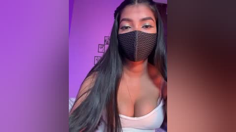 Video of a young woman with long black hair, wearing a black mask, a white off-shoulder top, and purple lighting.