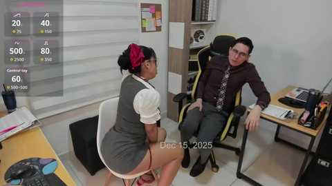 A video captures a tense office scene with a Black woman in a gray dress and a white man in a suit, both seated. The room features a computer screen displaying a timer, and a whiteboard with notes.