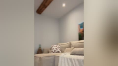 Blurry video of a modern, minimalist living room with beige sectional sofa, patterned pillows, wooden ceiling beams, and colorful abstract artwork on light gray walls.
