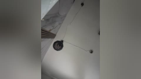 Video of a minimalist ceiling with white walls and a single, small, black ceiling light hanging from a thin, white cord. The light is centrally positioned, creating a simple, clean aesthetic.