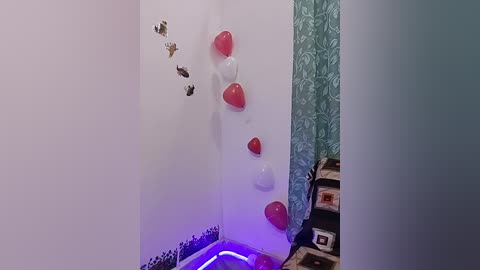 A video of a small, dimly lit room with white walls, a red heart-shaped balloon, and a few scattered black and white photos on a shelf.
