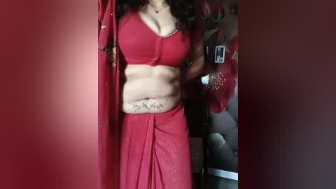 Video of a woman in a red sari, showing a toned, flat stomach with visible ribs and a tattoo on her lower abdomen.