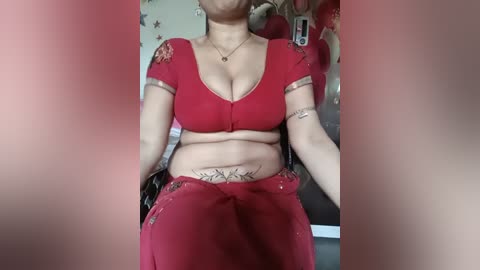 Video of a South Asian woman in a red sari, showcasing her medium-sized breasts and belly, seated against a floral wallpaper background.