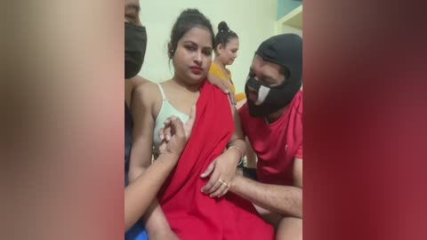 Video of a distressed woman in a red saree with a black mask, surrounded by people in casual clothing, possibly in a hospital setting.