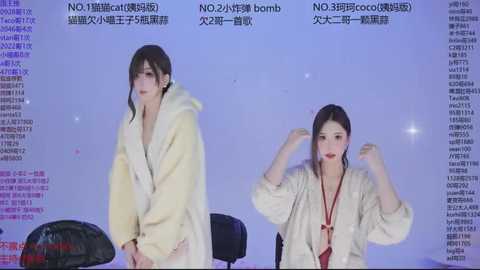 Video of two women in white robes, seated on a black chair, with a purple background displaying Chinese text. The woman on the left appears to be yawning, while the one on the right is smiling, adjusting her robe.