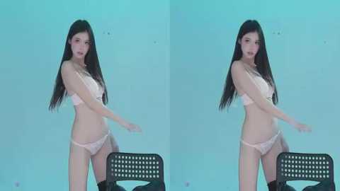 Video of a young East Asian woman with long black hair, wearing light pink lingerie, standing in front of a plain teal background.