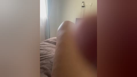 A video of a bedroom with soft lighting. The image is slightly blurred, focusing on a beige bed with a brown blanket. A wall-mounted light fixture is visible in the background.