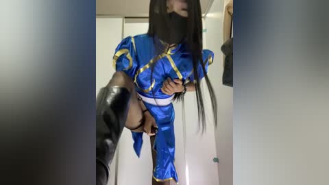 Video of a person in a blue and gold dragon costume with black boots and gloves, performing a kick. Background shows a white door and beige wall.