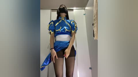 Video of a woman in a blue and gold cosplay outfit, exposing her black panties, standing in a narrow hallway with beige walls.