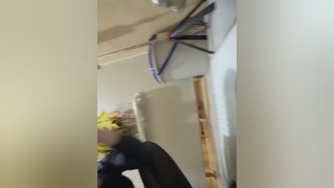 A blurry video of a person with a yellow mask and black clothing bending over, taken indoors with beige walls and a bamboo pole visible.