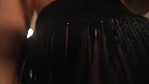 Video of a person's back, showing long, dark, straight hair parted down the middle. The background is blurred and dimly lit, emphasizing the glossy texture of the hair.