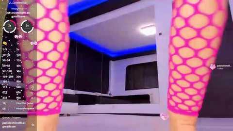 Video of a woman's legs in pink fishnet stockings and a black dress, captured in a modern, dimly-lit room with blue LED lighting, partially visible.