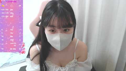 Video of a young Asian woman with long black hair, wearing a white off-shoulder dress, white face mask, and a black hair clip. She sits against a purple, starry background with a calendar.