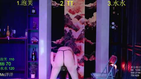 Video of a nude woman in a BDSM-themed setting, with a black blindfold and black thong. Background includes a large, abstract painting and dimly lit shelves with bottles. Text overlays indicate live stream details.
