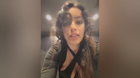 Video of a young woman with medium brown skin and curly dark hair, wearing a black top, captured from a close-up angle, indoors.