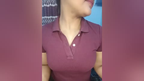 Video of a woman wearing a burgundy polo shirt with a small button-down collar. The background features a striped patterned wall and a blue wall.