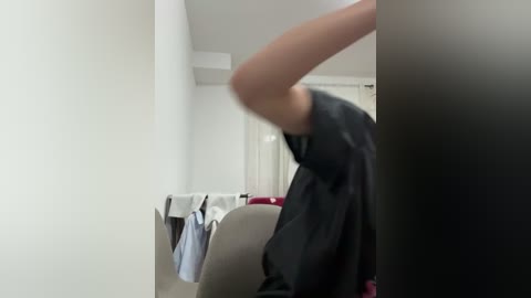 A blurry video of a person in a black shirt leaning against a wall in a dimly lit room with white walls and a bed with white and red sheets.