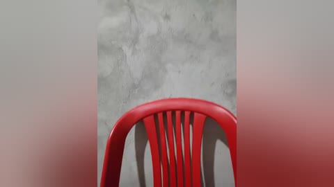Video of a vibrant red plastic chair with a ribbed backrest against a textured, gray concrete wall. The background fades from gray to pink, creating a subtle gradient. The image captures a minimalist, modern aesthetic with a focus on contrasts.
